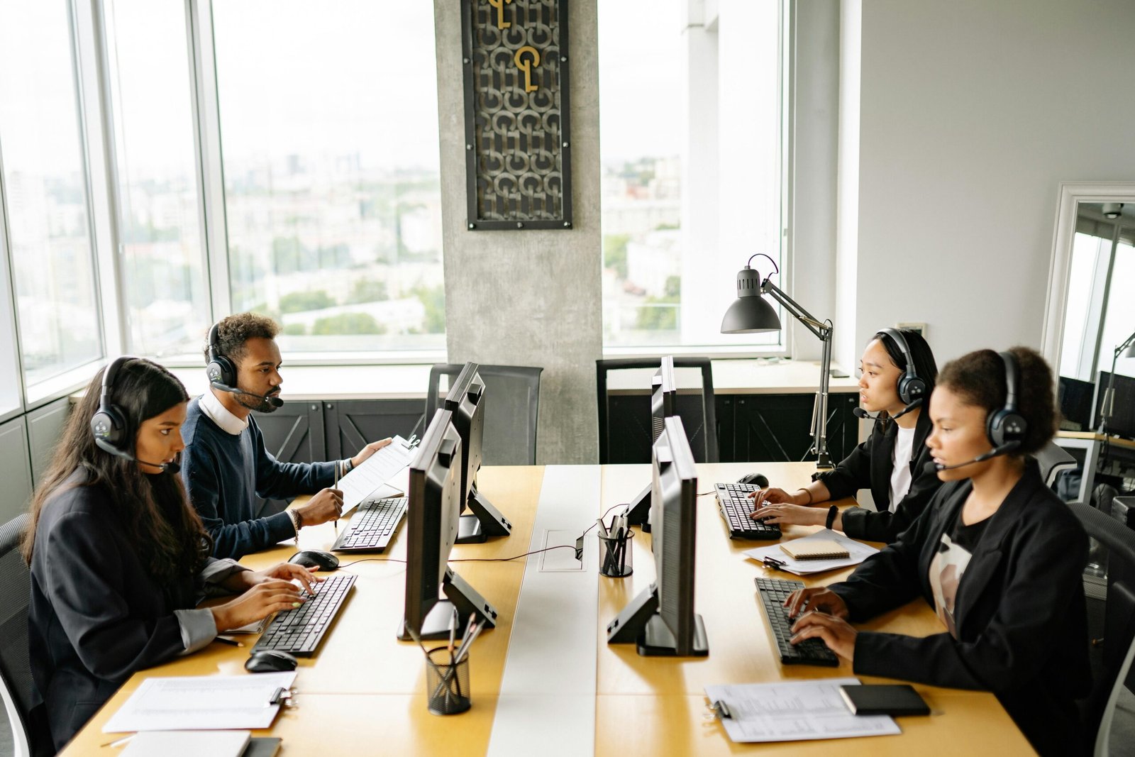 Vier medewerkers van een klantenservice team dragen headsets en werken geconcentreerd achter hun computers in een modern, licht kantoor