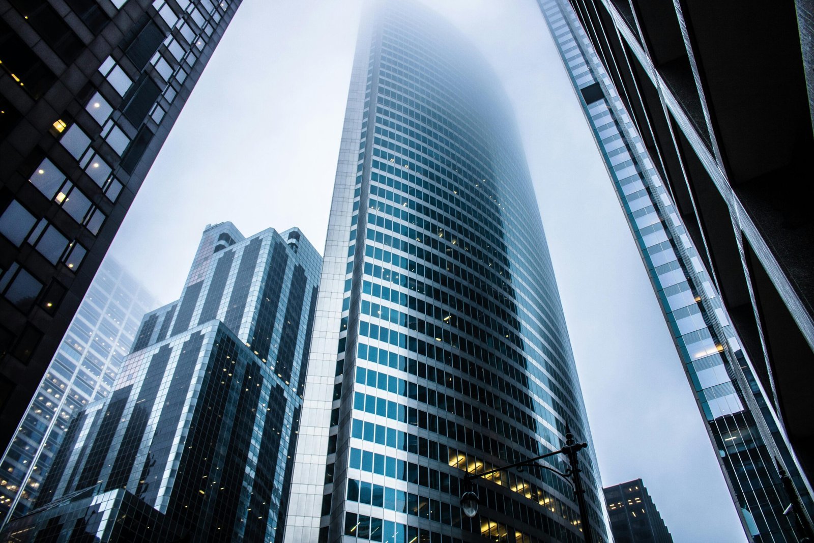 Een indrukwekkend kikvorsperspectief van moderne glazen kantoorpanden die verdwijnen in de mist, symbool staand voor de transitie en schaalbaarheid in de zakelijke dienstverlening.