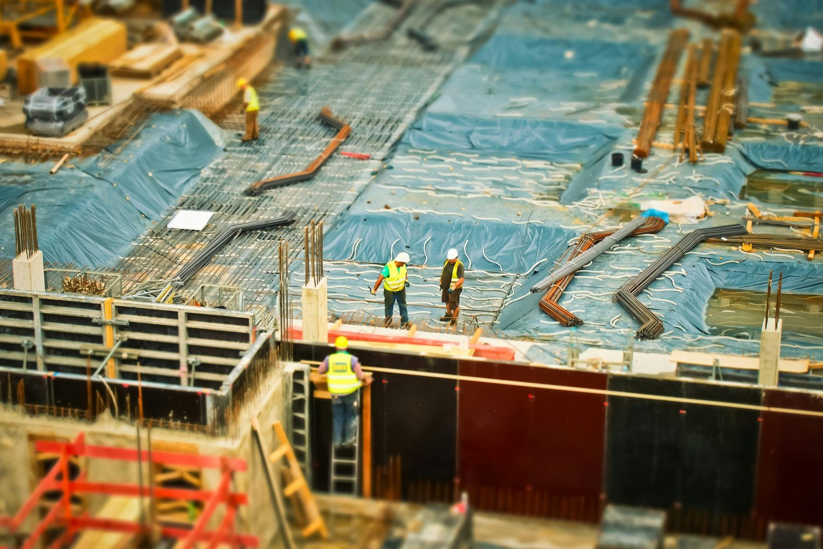 Een bovenaanzicht van een actieve bouwplaats met bouwvakkers in veiligheidsvesten die werken aan de fundering en bewapening, gebruikt als illustratie voor efficiëntie en AI-toepassingen in de bouwsector.