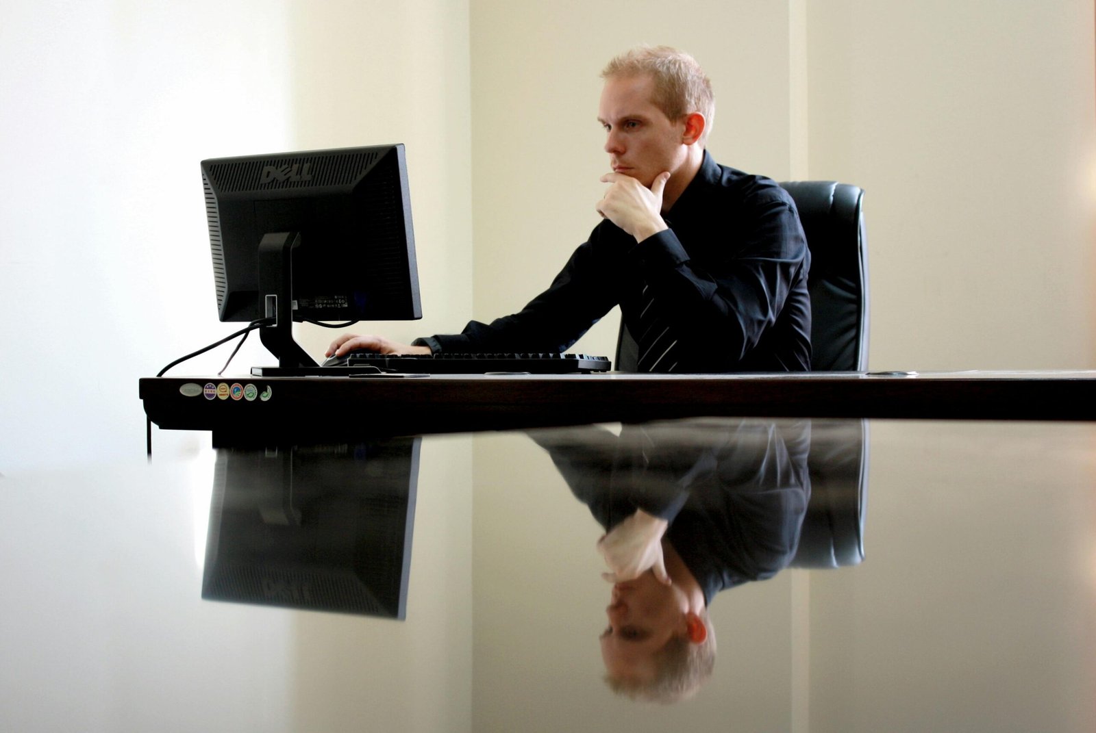 Een man in een zwart overhemd zit geconcentreerd achter een computer aan een bureau met een weerspiegelend tafelblad, werkend aan verkoopautomatisering.